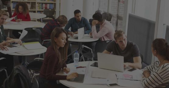 A library filled with students around a table discussing web design ideas.